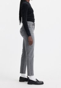 Vaqueros altos de cintura en gris con pierna recta, combinados con un suéter de punto negro difuso y mocasines negros sobre calcetines blancos.