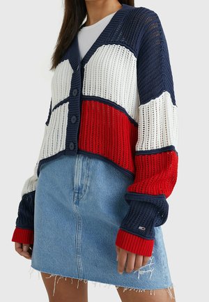 Knit cardigan in navy, white, and red. Features V-neck, button front, and ribbed cuffs. Paired with a light denim mini skirt.