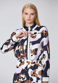 Robe à manches longues avec fermeture à boutons, présentant un motif floral abstrait dans des tons de marine, marron et lavande sur fond blanc. Taille élastique et col.