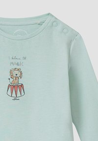 Lichtblauw langemouw t-shirt gemaakt van zacht katoen. Heeft een cartoonleeuw op een trommel met de tekst "Ik geloof in magie." Drukknopen op de schouder.