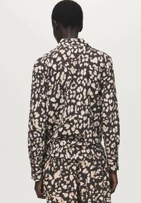 Majica z dolgimi rokavi iz mehke tkanine, z rjavim osnovnim odtenkom in bež ter belim abstraktnim vzorcem leopardjega potiska, zasnovana za sproščen kroj.