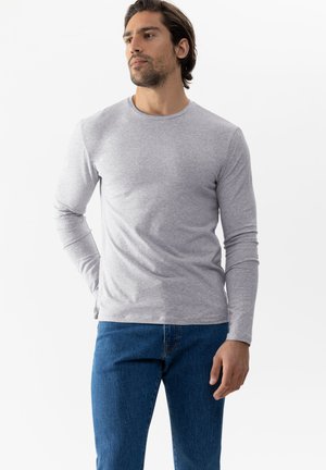 Maglietta grigia a maniche lunghe realizzata in tessuto morbido, con scollatura rotonda, abbinata a jeans blu. La maglietta ha una superficie liscia e una vestibilità comoda.