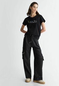 T-shirt nera con logo "Liu Jo" in colori vari e pantaloni cargo neri oversize con un motivo texture, dotati di tasche e vita con cordino.