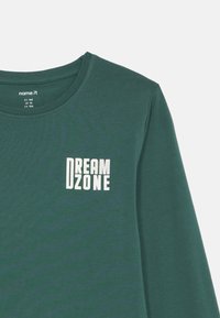 Dark green long-sleeve shirt with white text "DREAM ZONE" on the left chest and size label "name it" inside the collar.