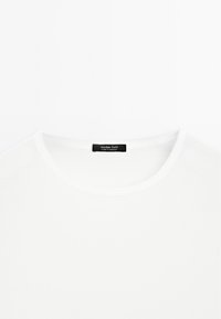 Weißes Baumwoll-T-Shirt mit rundem Hals, das eine glatte Textur aufweist und ein schwarzes Etikett innen mit dem Markennamen "Massimo Dutti" trägt.