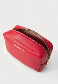 Red leather cosmetic bag with a gold zipper and logo, featuring a rounded design, smooth texture, and a beige interior lining.