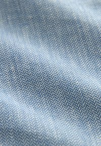 Tissu bleu clair présentant un motif en chevrons, mettant en valeur une texture lisse avec un subtil éclat et de fins fils contrastants.