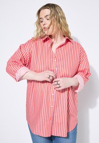 Camisa de botones a rayas rojas y blancas con cuello, mangas largas y puños enrollados. Tejido suave con un ajuste ligeramente holgado.