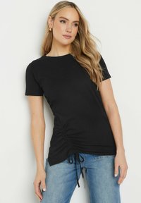 T-shirt nero a maniche corte con dettagli arricciati ai lati e lacci regolabili nell'orlo. Realizzato in un tessuto morbido e liscio. Vestibilità casual e scollatura rotonda.