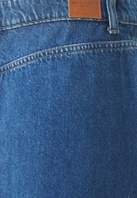 Kék farmernadrág sima textúrával, bőr cimkével a derékrészen, amelyen az "ONLY BLUE DENIM" felirat olvasható. Érzékelhető varrások.