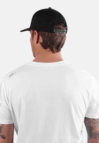 T-shirt en coton blanc avec un col rond, des manches courtes et une petite étiquette noire sur l'épaule. Associé à une casquette noire ajustable.