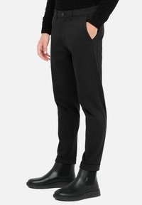 Black cotton-chino pants with a button waistband, side pockets, and a tapered fit, paired with shiny black ankle boots.
