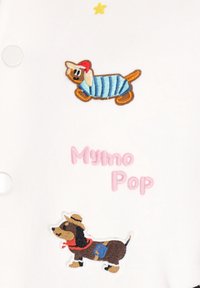 Fehér szövet, amelyen két hímzett tacskó látható. Az egyik kék csíkos inget és piros kalapot visel, a másik pedig cowboy kalapot és kendőt.