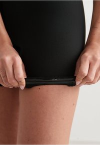 Pantalones cortos negros hechos de un material elástico, con una cinturilla negra brillante. La prenda está siendo tirada ligeramente en la zona del muslo.