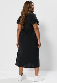 Czarna, prążkowana sukienka midi z rozkloszowanymi rękawami i elastyczną talią. Noszona z białymi trampkami, cechuje się luźnym krojem i gładką fakturą.