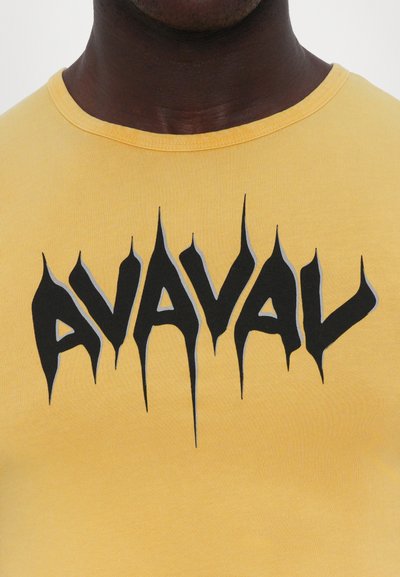 Gul bomulds t-shirt med en fremtrædende sort grafisk tekst "AVAL" med skarpe, takkede kanter og grå accenter på bogstaverne.
