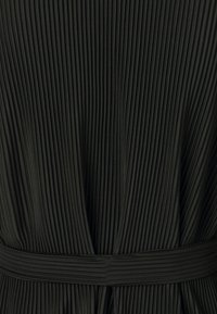 Robe en tissu noir plissé avec des rainures verticales, une taille marquée et une texture lisse. Le design met en avant le flux et le mouvement.