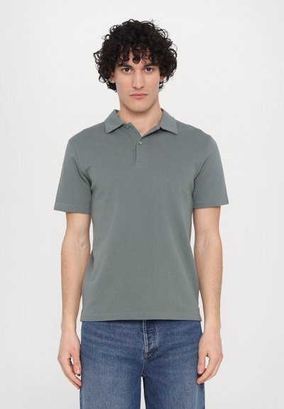 Polo gris avec un col, des manches courtes et un tissu texturé, associé à un jean bleu. Deux boutons au col.
