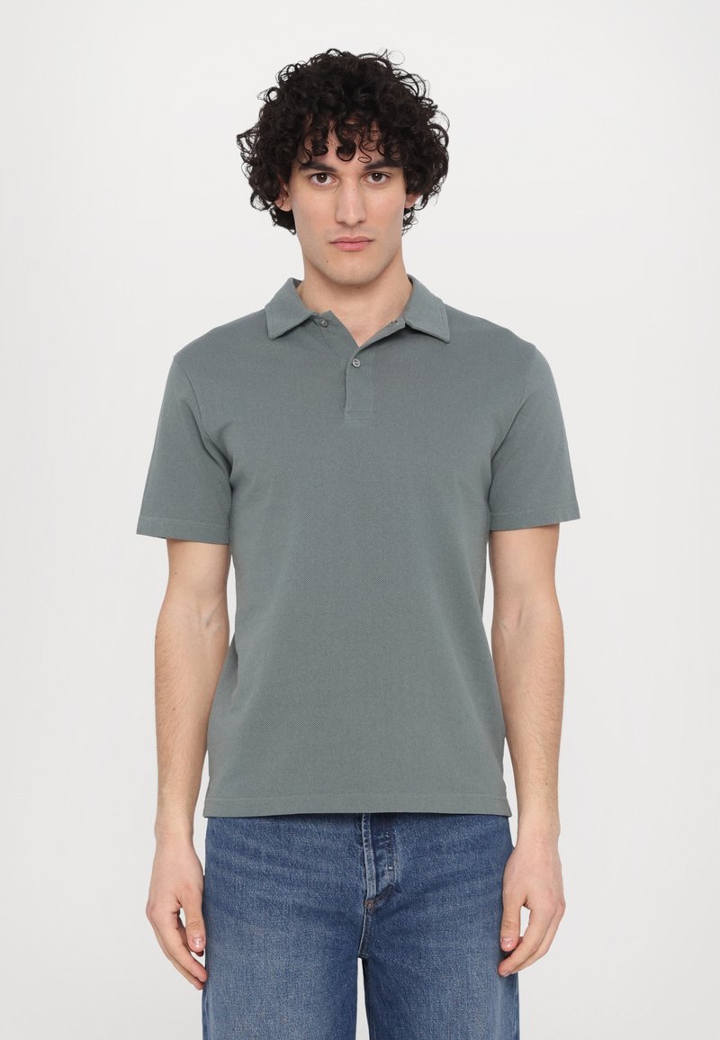 Gray polo shirt with a collared neckline, short sleeves, and a textured fabric, paired with blue jeans. Two buttons at the collar.