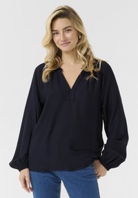 Blusa blu navy con scollatura a V, dettagli arricciati sulle spalle e maniche lunghe voluminose con polsini elasticizzati, realizzata in un tessuto leggero.