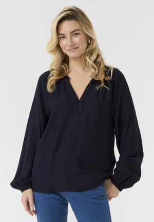 Blouse bleu marine avec un décolleté en V, des détails froncés aux épaules et des manches longues volumineuses avec des poignets élastiques, fabriquée en tissu léger.