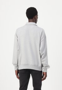 Pullover cinza de mangas longas com colarinho. Feito de um material suave e texturizado. Apresenta um corte relaxado e punhos canelados. Vista traseira mostrada.