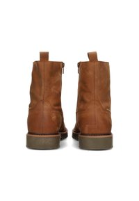 Botas de cuero marrón hasta el tobillo con un acabado suave, cremallera trasera y acentos de costura. Suela de goma gruesa que proporciona tracción. Buclera corta.