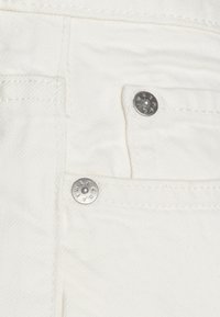 Tissu en denim blanc avec une texture en chevron distincte. Présente deux boutons en métal argenté avec du texte et des détails de couture visibles.