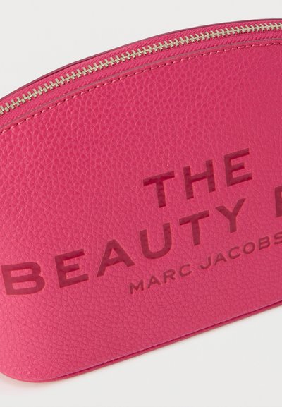 Κοντινό πλάνο σε ροζ υφασμάτινο νεσεσέρ με φερμουάρ, με την επιγραφή «THE BEAUTY» και μικρότερα γράμματα «MARC JACOBS» από κάτω.