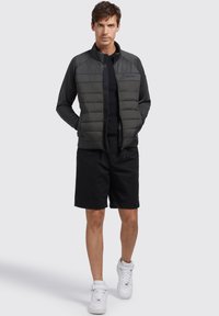 Padded gray jacket with a smooth, dark gray upper section, a zip closure, and long sleeves, paired with black shorts and white sneakers.