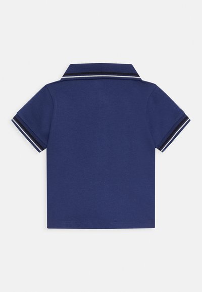 Polo azul marino, de mangas cortas, con cuello plano. Presenta detalles a rayas en blanco y azul oscuro en el cuello y los bordes de las mangas.