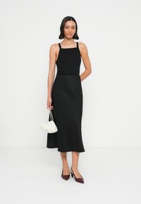 Haut noir sans manches avec encolure carrée, associé à une jupe midi noire. Accessoires : un sac crème et des chaussures à talons hauts bordeaux.