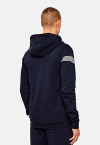 Felpa con cappuccio blu navy con finitura testurizzata, dotata di cappuccio e dettagli a strisce bianche sulle spalle. Maniche lunghe e vestibilità comoda.