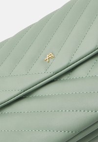 Clutch de cuero verde con patrón de acolchado diagonal, que presenta un logotipo de hardware dorado. Textura suave y diseño plegado con un sutil detalle de costura.