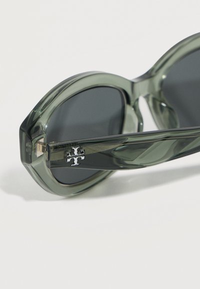 Χοντρά διάφανα γκρι γυαλιά ηλίου με στρογγυλεμένους σκελετούς και σκουρα φακούς, με ένα μικρό ασημί λογότυπο στο πλαϊνό μέρος του βραχίονα.