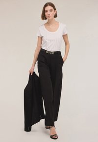 Hvid kortærmet ribbet t-shirt, højttaljede sorte vide bukser med et guld bælte, og sorte remsandaler. Sort blazer hængende over armen.