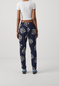 Navy floral-print trousers with an elastic waistband, featuring large cream flowers, paired with blue shoes. Simple fitted white top.