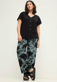 Černý proužkovaný top s krátkými rukávy a předními knoflíky, zkombinovaný s širokými kalhotami s modro-černým tie-dye vzorem. Černé platformové boty.