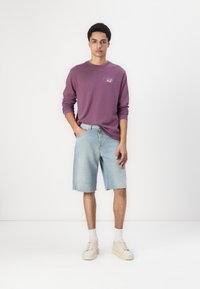Purple long-sleeve shirt with "Star Wars" logo, paired with light blue denim shorts featuring frayed hem and distressed details, and beige sneakers.