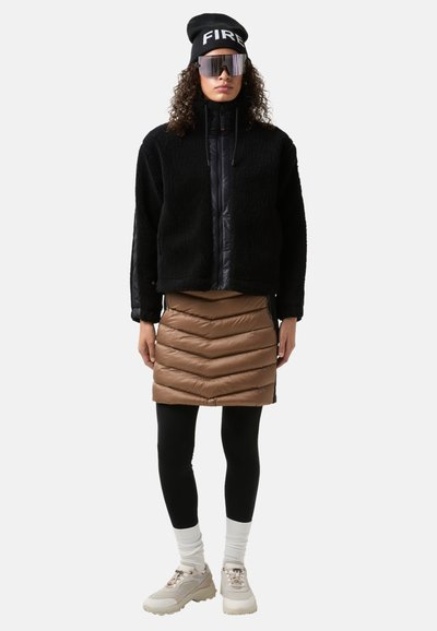 Black fleece jacket with a high collar, brown puffer skirt with chevron design, black leggings, white socks, and chunky cream sneakers.