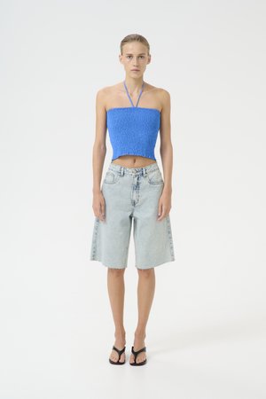 Blå smocket crop-top med halter-stropper, parret med lyseblå denim bermuda-shorts og sorte flip-flops. Ren, minimalistisk æstetik.