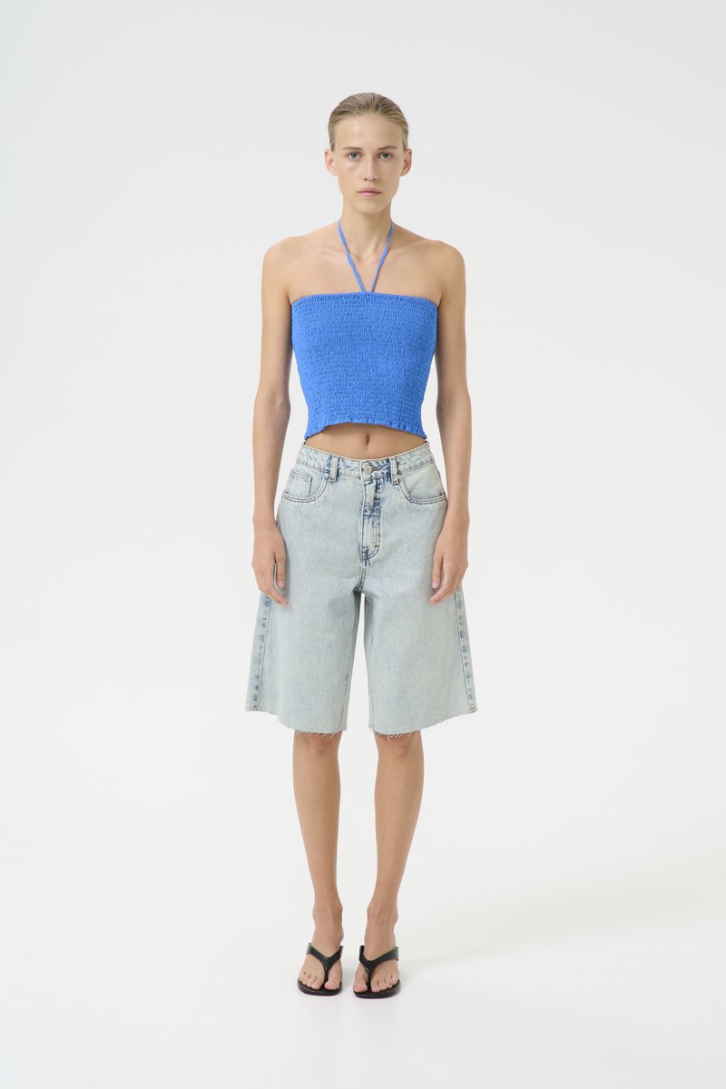 Plavi smockani top s halter trakama, uparen s svijetloplavim traper bermudama i crnim japankama. Čista, minimalistička estetika.