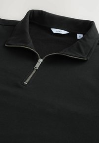 Sort pullover med lynlås krave, lavet af glat stof. Har en sølv lynlås og et mærke, der angiver størrelse medium.