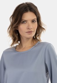 Jasnoniebieska, gładka bluzka z długimi rękawami i okrągłym dekoltem. Prosty fason bez widocznych wzorów czy akcentów.