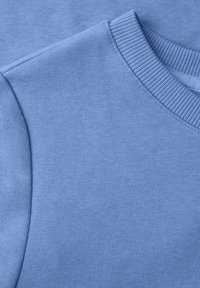 Gros plan sur un tissu tricoté bleu clair montrant l'encolure et la couture d'épaule d'un vêtement.