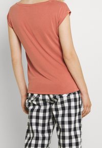 Top corto color ruggine con scollatura ampia, abbinato a pantaloni a quadri bianchi e neri con vestibilità comoda e trama morbida.