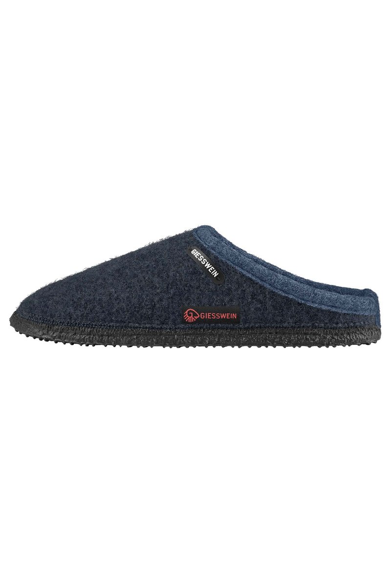 Donkerblauwe vilten slipper met een gestructureerd oppervlak, ronde neus, zwarte rubberen zool en een klein merketiket met rode accenten.