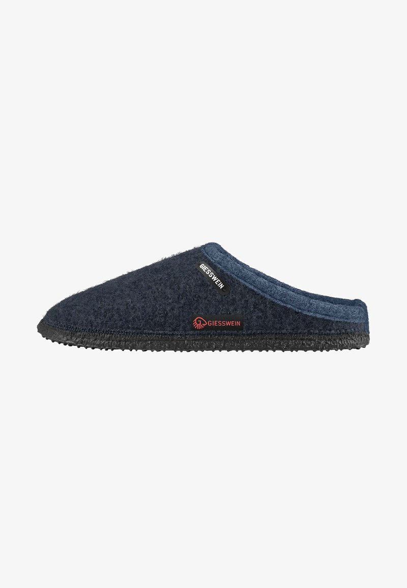 Donkerblauwe vilten slipper met een gestructureerd oppervlak, ronde neus, zwarte rubberen zool en een klein merketiket met rode accenten.