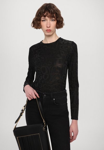 Top negro de manga larga con un patrón texturizado y transparente. Combinado con unos vaqueros negros de cintura alta y un bolso negro estructurado con detalles en dorado.