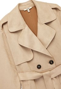 Beige trench coat med brede klapper, dobbelt sorte knapper, et matchende bælte og en brun inderside.